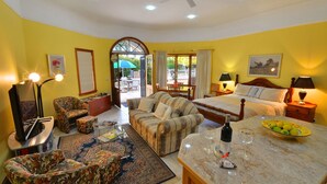 A hotel room with a bed, two sofas, a dining table, a TV, and a balcony with a view.