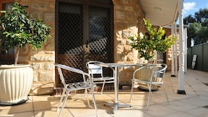 An outdoor patio with two metal chairs and a table, a stone building with a metal gate, and potted plants.