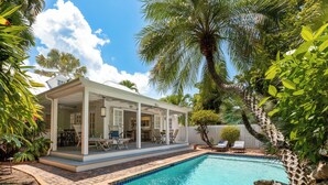 Un patio couvert avec des meubles d’extérieur, une piscine et une végétation luxuriante.