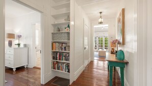 Un couloir avec une bibliothèque blanche, un plancher en bois et une table turquoise sur laquelle est posé un vase.