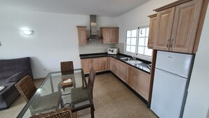 Uma cozinha compacta com armários de madeira, uma mesa de jantar de vidro e micro-ondas embutido.