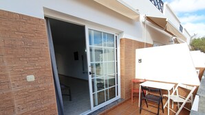 Um pátio com mesa, cadeiras, uma porta de vidro deslizante e chão revestido de azulejos.