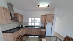 Cozinha moderna com armários de madeira, bancada preta, mesa de jantar de vidro, cadeiras de vime, micro-ondas e geladeira.