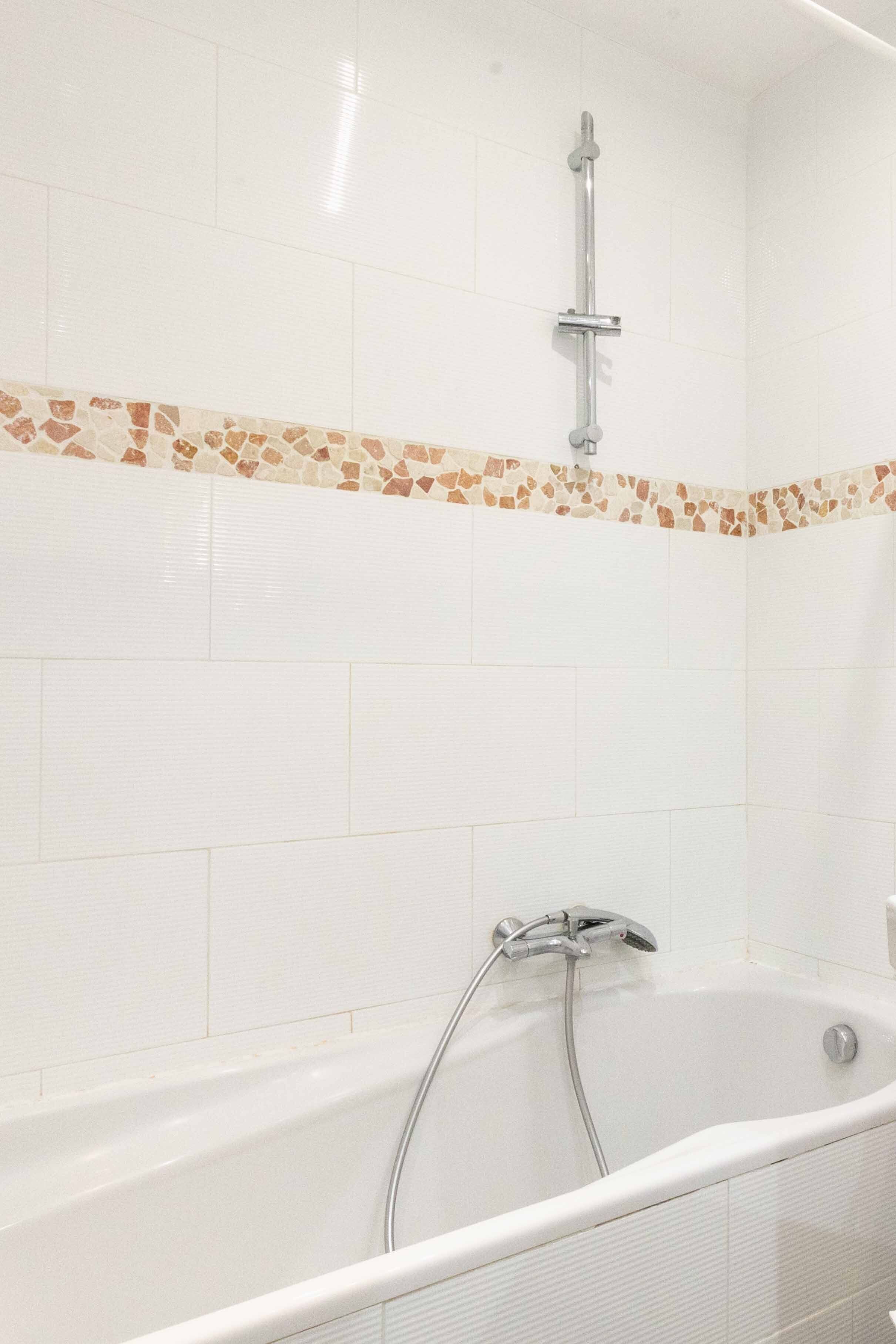 A bathroom with a bathtub, a shower, and a mosaic tile border.