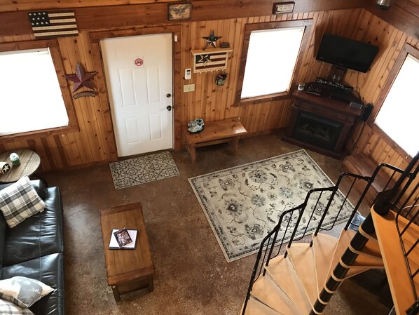 A cabin interior with a wooden floor, a sofa, a coffee table, a rug, a bench, a fireplace, and a TV. - Cozy Fireside Cabin, Great for Couples, Families and Outdoorsmen! (McArthur)