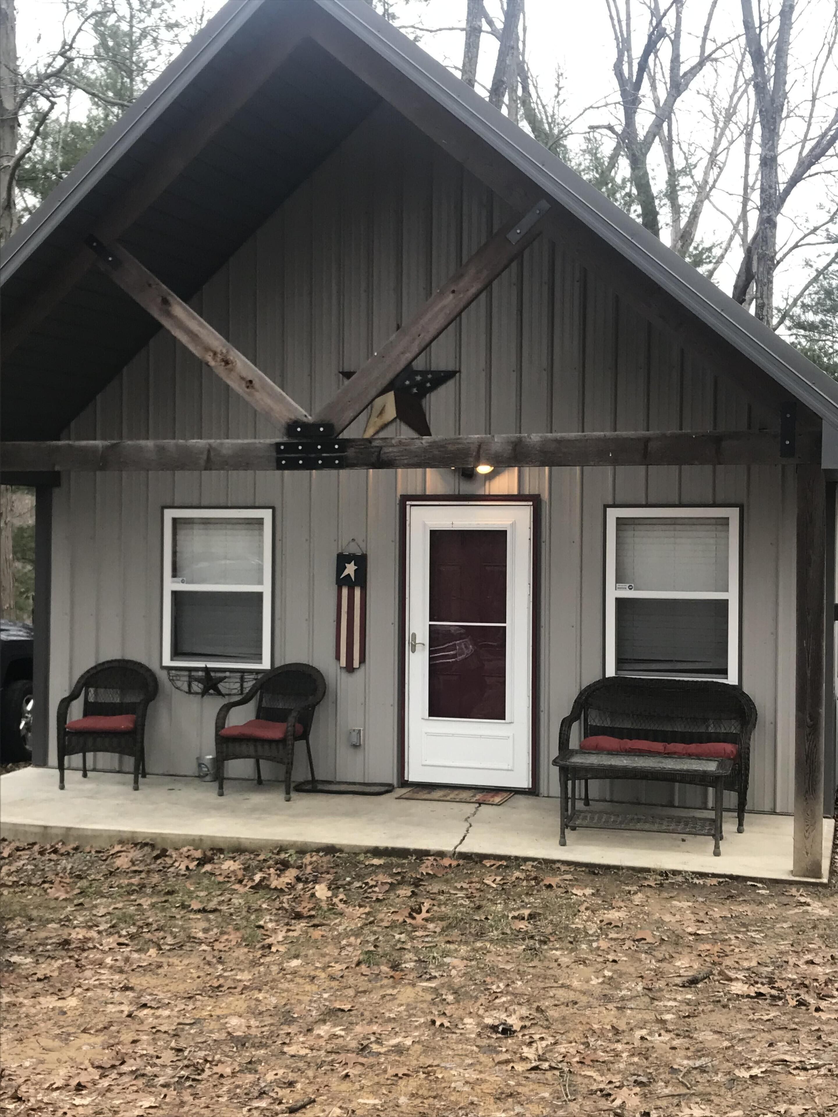 A small, single-story building with a sloped roof, a front door, and two windows. There are two chairs with red cushions in front of the building.