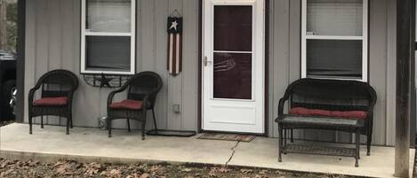 A small, single-story building with a sloped roof, a front door, and two windows. There are two chairs with red cushions in front of the building.