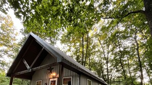 Une cabane rustique avec un toit en pente, une véranda avec des chaises et une allée gravillonnée.