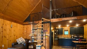 Un vaste espace de vie aménagé dans un style industriel, avec un lit en mezzanine, un escalier, un coin cuisine et une table à manger.