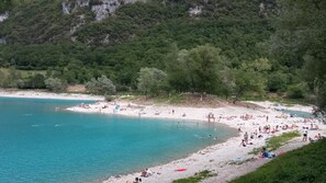 A beach with people sunbathing and swimming, surrounded by trees and hills.