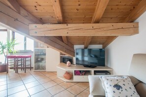 Un salon doté d’un plafond en bois, d’un téléviseur à écran plat posé sur un meuble de télévision blanc, d’un canapé beige et d’un coin repas avec une table et des chaises.