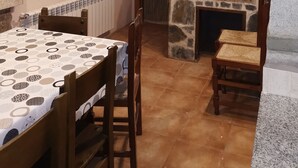 A cozy dining area with a stone fireplace, a table with a patterned tablecloth, and wooden chairs. - Los Corzos Burgohondo Avila (Burgohondo)