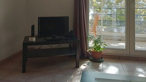 Una habitación con televisión sobre un mueble bajo, una planta en maceta y un ventanal corredero que da a un espacio exterior.