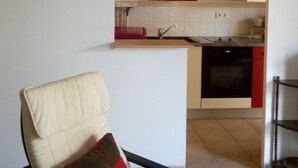 Un salón con una silla y vistas a una cocina a través de un arco.