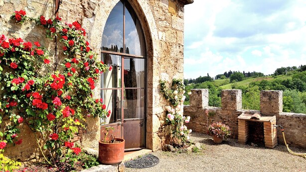 A stone building with a large arched window, a brick oven, and a garden with red flowers. - Panoramic castle with large pool on the walls. Ideal for weddings and events (Poggibonsi)