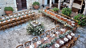 An outdoor dining area with multiple tables set for a meal, surrounded by stone walls and potted plants. - Panoramic castle with large pool on the walls. Ideal for weddings and events (Poggibonsi)