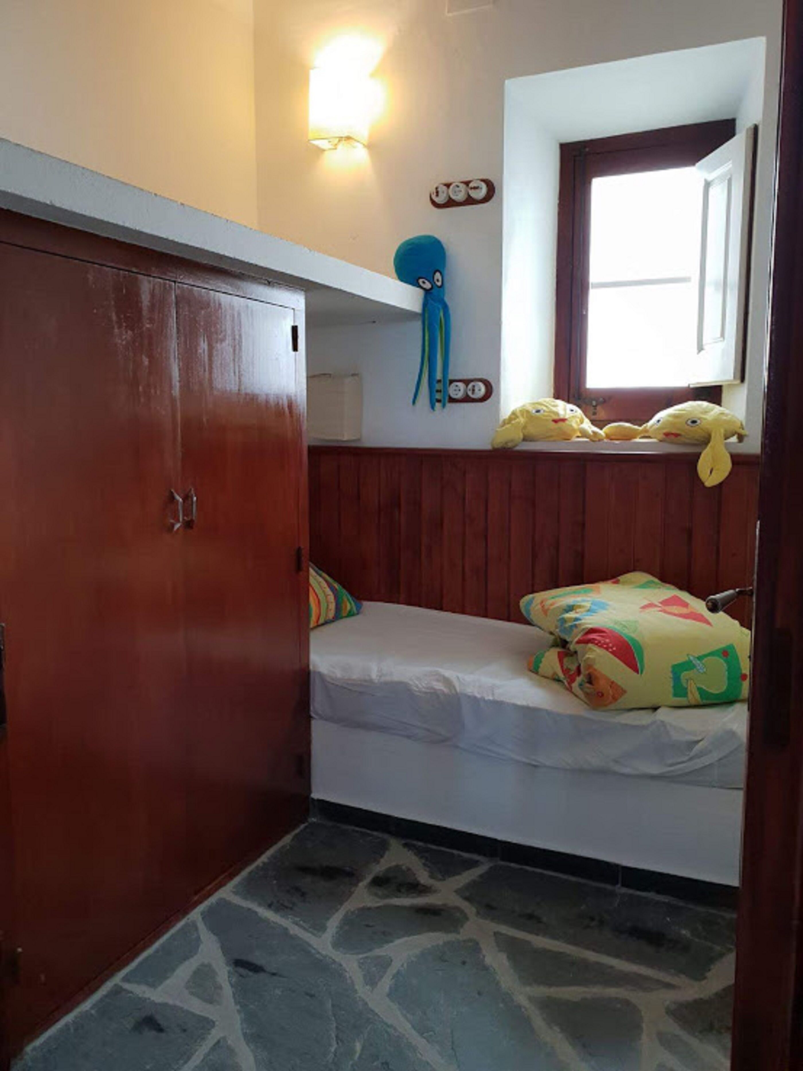 A small, compact room with a bunk bed, a wardrobe, a wall-mounted light, and a window with a view.