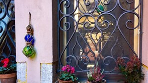 A window with ornate metalwork, potted plants, and decorative figurines on a ledge. - Ca' Venexiana, quiet 2 bedroom with private canalside courtyard - no added fees! (Venezia)