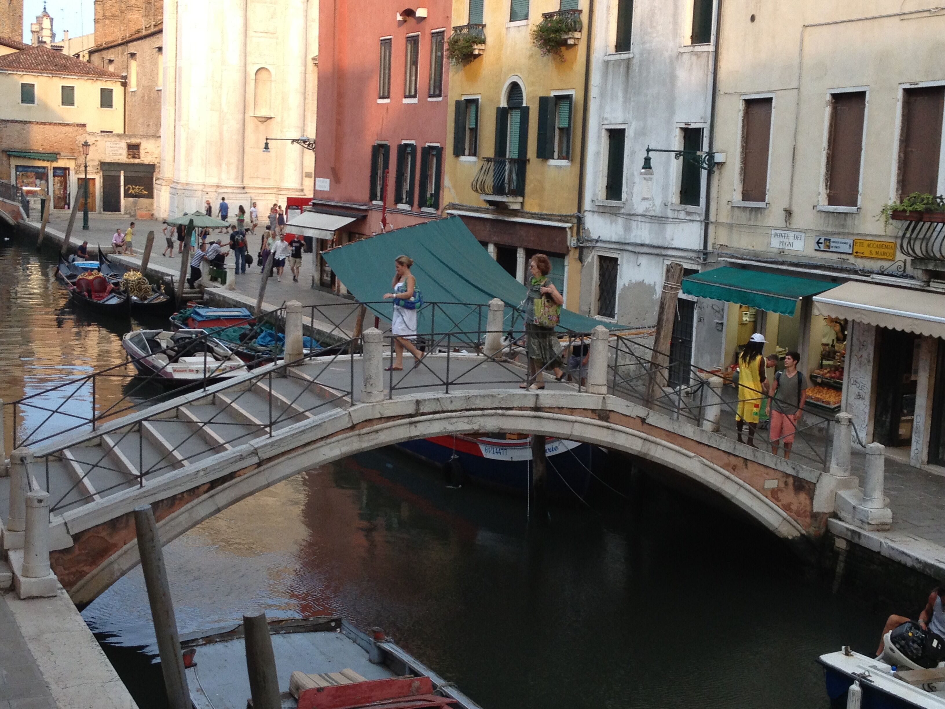 Un canal con barcos, un puente peatonal y edificios con tiendas.