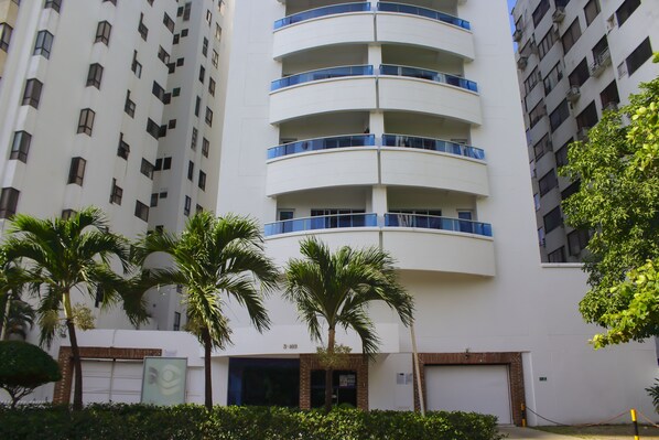 A multi-story building with balconies, palm trees, and a garage entrance.