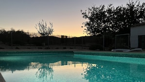 Ein Schwimmbecken mit klarem, blauem Wasser, umgeben von einem Zaun und Bäumen, im Abendlicht.