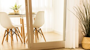 Zona de menjador amb una taula preparada per a dues persones, una planta en test i una vista a través d'una porta de vidre.