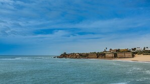 Paisatge costaner amb un promontori rocos i edificis sobre una platja sorrenca.