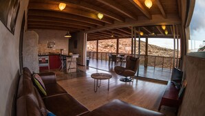 Un interior moderno con techo de madera curvada, una zona de estar acogedora, una cocina y un espacio comedor con vistas a terreno rocoso.