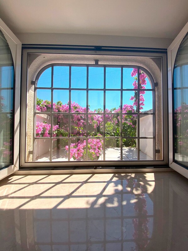 A room with a large arched window, a tiled floor, and a view of pink flowers outside.