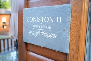 Een grijze bord met de tekst 'CONISTON 11 DAISY LODGE' en een bloemenmotief.