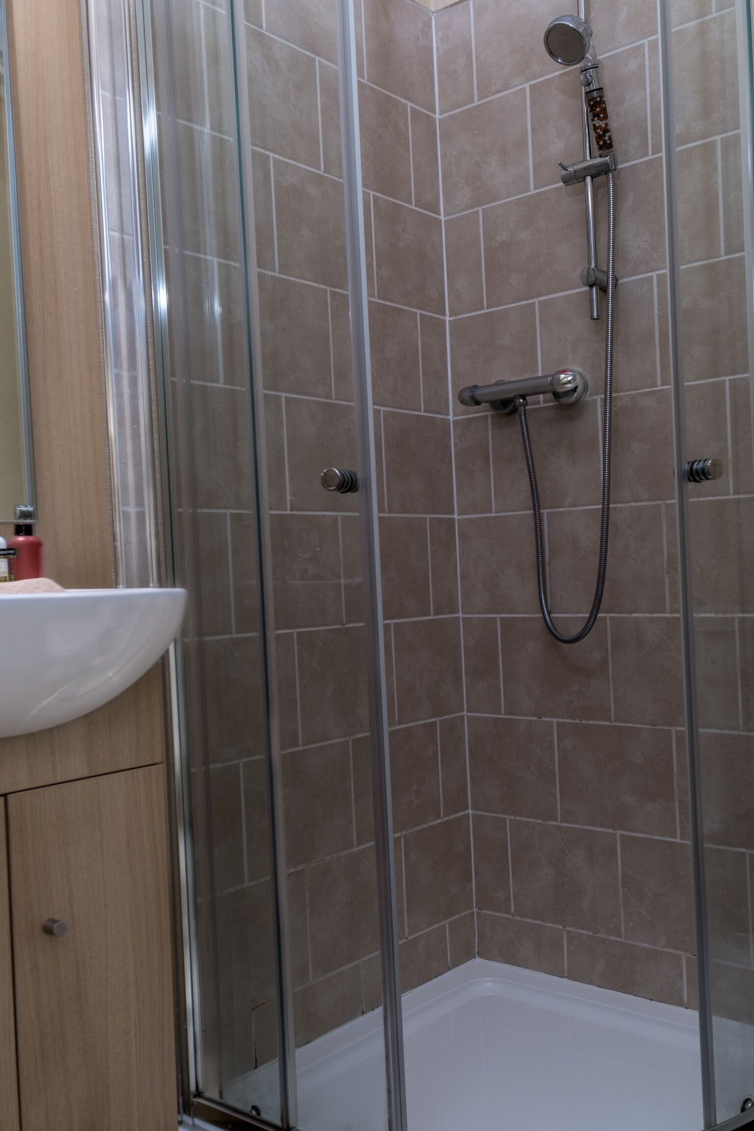 A glass-enclosed shower with a handheld showerhead and a handheld hose.