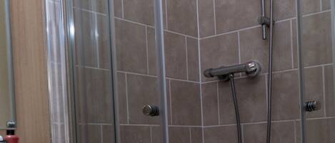 A glass-enclosed shower with a handheld showerhead and a handheld hose.