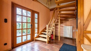 Una escalera de madera que conduce a un piso superior, un amplio ventanal con vistas a árboles y un radiador en el suelo.