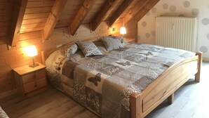Un dormitorio acogedor con techo de madera, cama con ropa de cama estampada, dos lámparas de noche y un radiador.