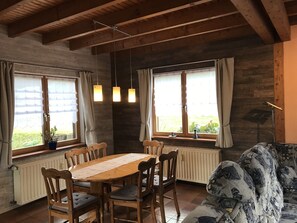 A cozy dining area with a wooden table and chairs, large windows with curtains, and a radiator below.