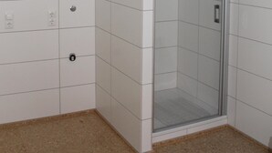 A bathroom with white tiled walls, a glass shower enclosure, and a beige floor. - House Roy, 3 room apartment in the redeveloped house  (Zülpich)