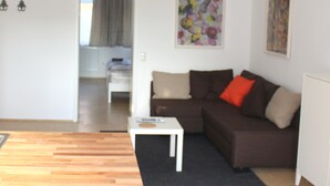 A modern living room with a brown sofa, a white coffee table, and a black rug. There is a painting on the wall and a door leading to another room. - House Roy, 3 room apartment in the redeveloped house  (Zülpich)