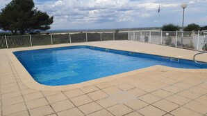 Una piscina rectangular amb una terrassa enrajolada, envoltada per una tanca blanca, i un penya-bàns a la part posterior.