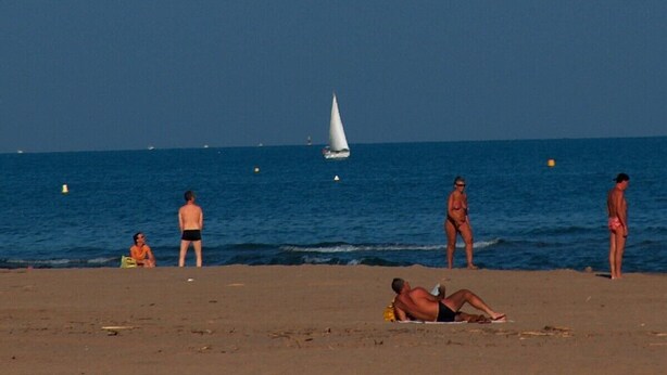 Escena de platja amb persones que prenen el sol i es passegen vora l'aigua.