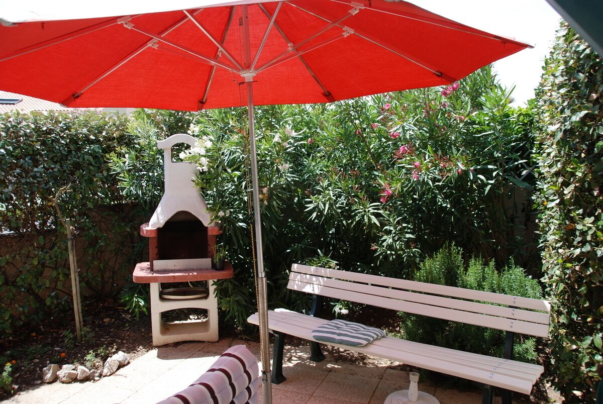Un patio al aire libre con un paraguas rojo, un banco blanco y un horno de pizza.