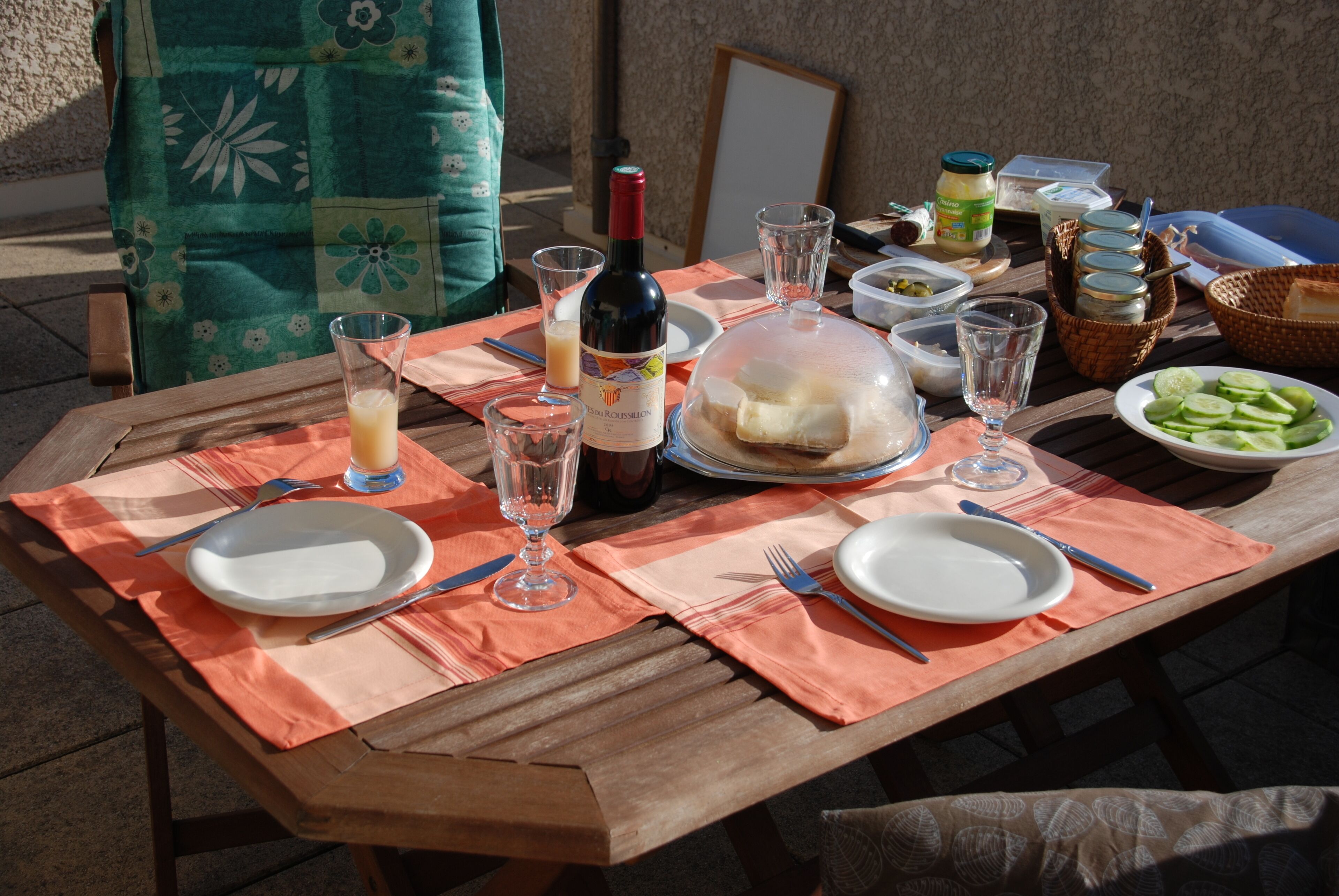 Ein Holztisch ist für eine Mahlzeit gedeckt, mit Tellern, Besteck, einer Weinflasche und verschiedenen Speisen.