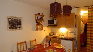 A dining area with a table set for two, a microwave, and a small kitchen area with a sink and cabinets. - Ground level for 4 pers, superb setting 164 yards from the ski runs et the shops (Les Deux-Alpes)