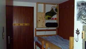 A small, compact room with a bunk bed, a wooden door, and a wall-mounted shelf with personal items. - Ground level for 4 pers, superb setting 164 yards from the ski runs et the shops (Les Deux-Alpes)