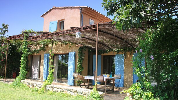 Une maison avec un patio couvert, une table et des chaises, et un jardin.