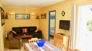 Una sala de estar con sofá, sillas, una mesa de comedor con un bol y televisor.