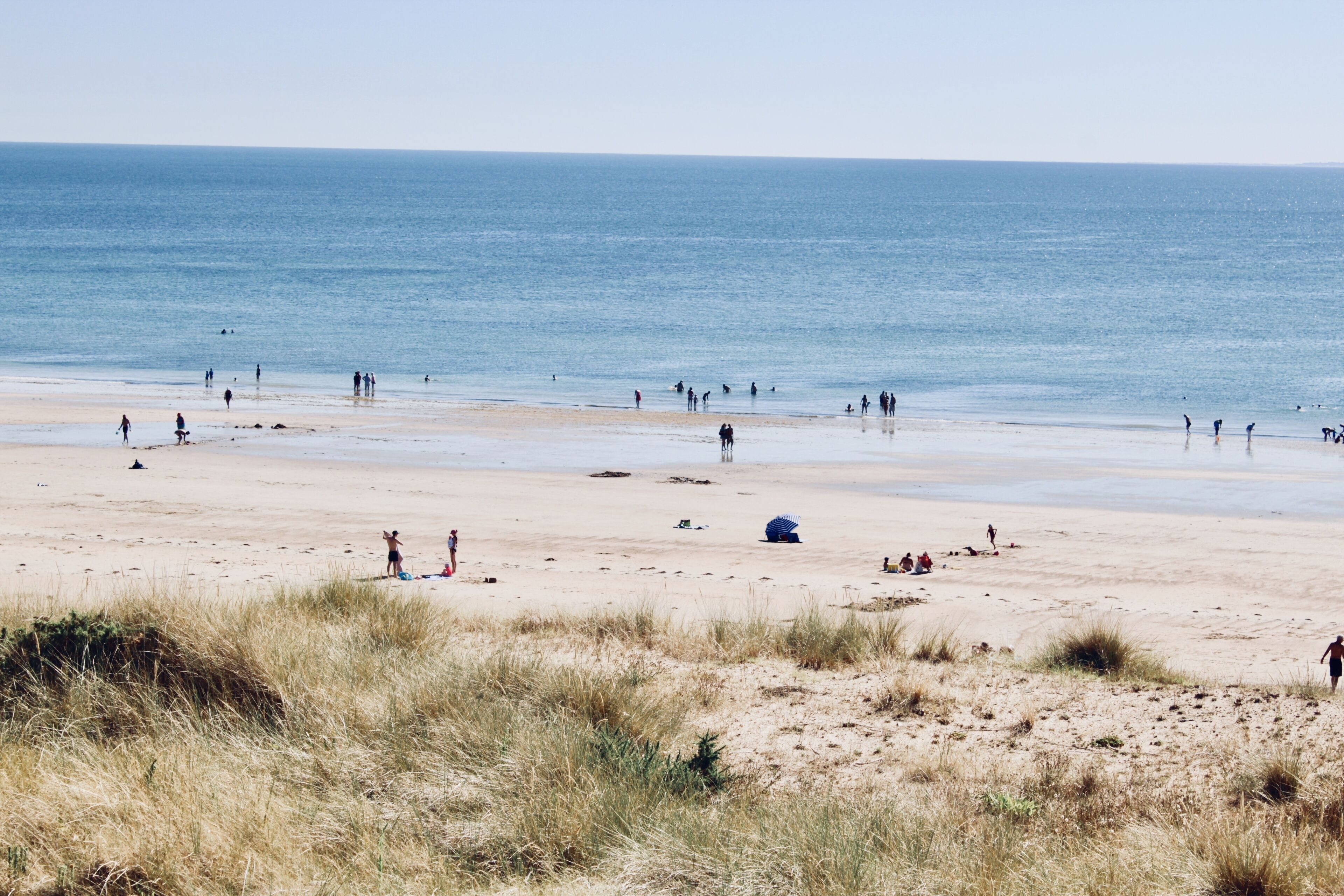 A beach with people walking and sitting, and a clear view of the ocean.