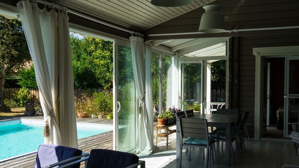 Ein überdachter Außenbereich mit Pool, Sitzgelegenheiten und einem Tisch.