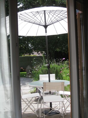 An outdoor patio with a table and chairs, a large umbrella, and a garden with various plants and flowers.