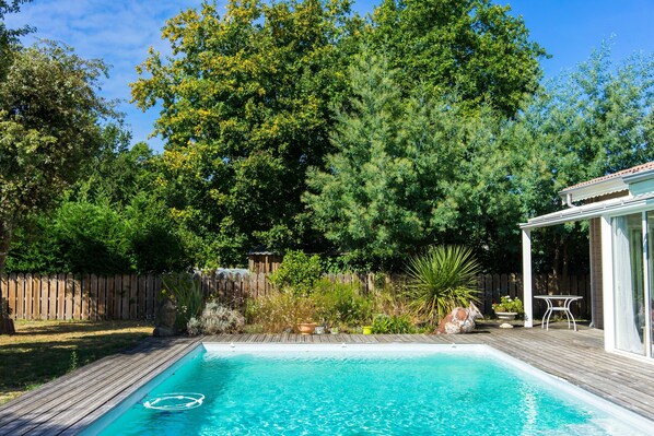 A swimming pool with a wooden deck, surrounded by trees and a wooden fence.