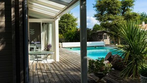 Eine Holzterrasse mit Pool, einer überdachten Terrasse und einem Gartenbereich mit Pflanzen.